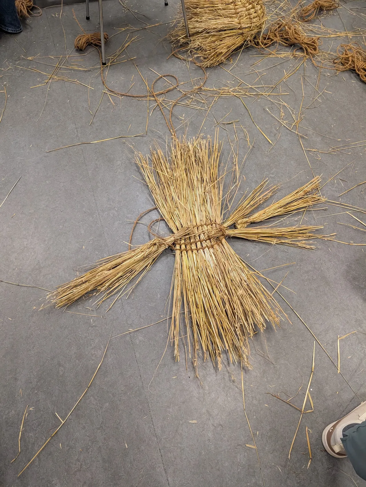 You need to clean the straw a lot more than with the Skekler’s hats (mostly because the hats were much faster / single-use and kind of look cool when they’re messy, but the baskets with extra leaves or hulls will more likely rot). You twine 10 of the 14 bundles into a mat similar to the hats, except in the middle instead of at the end, and then you use the remaining four (two per side) folded in half as the space / shape pieces that give the basket its triangular cross section.